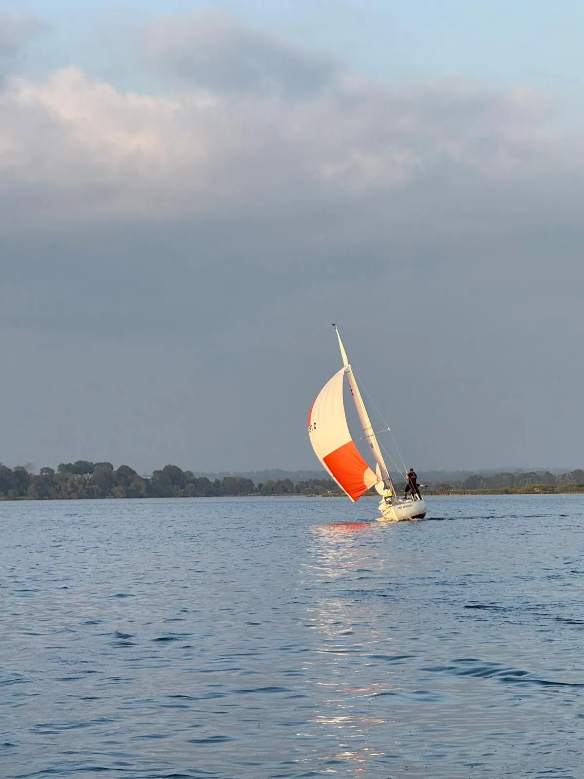 A keelboat running downwind under spinnaker on Lough Neagh at golden hour